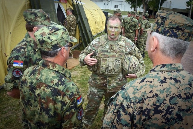 A man in military camouflage uniform speaking to three other army men