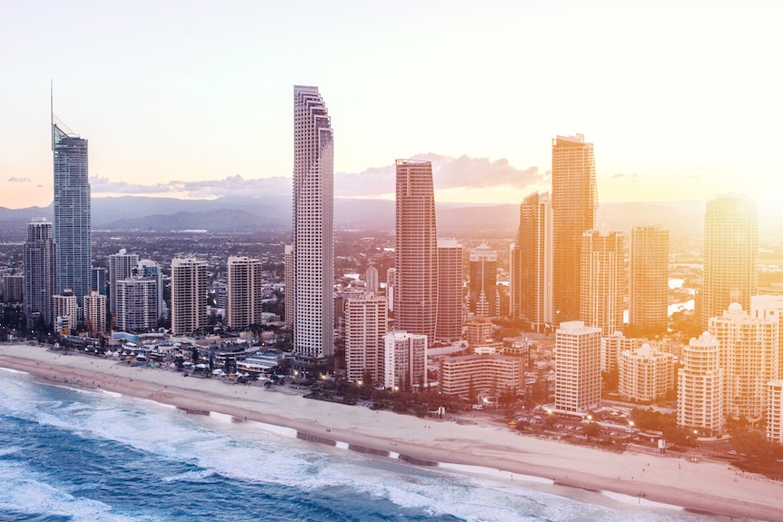 Surfers Paradise sky-line at sunset with beach front and waves crashing on sand.