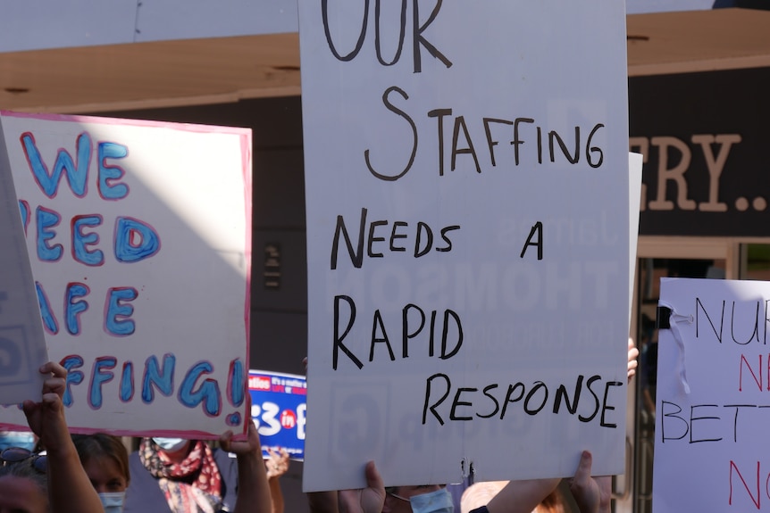 a nurse holds up a sign saying 'our staffing needs a rapid response'