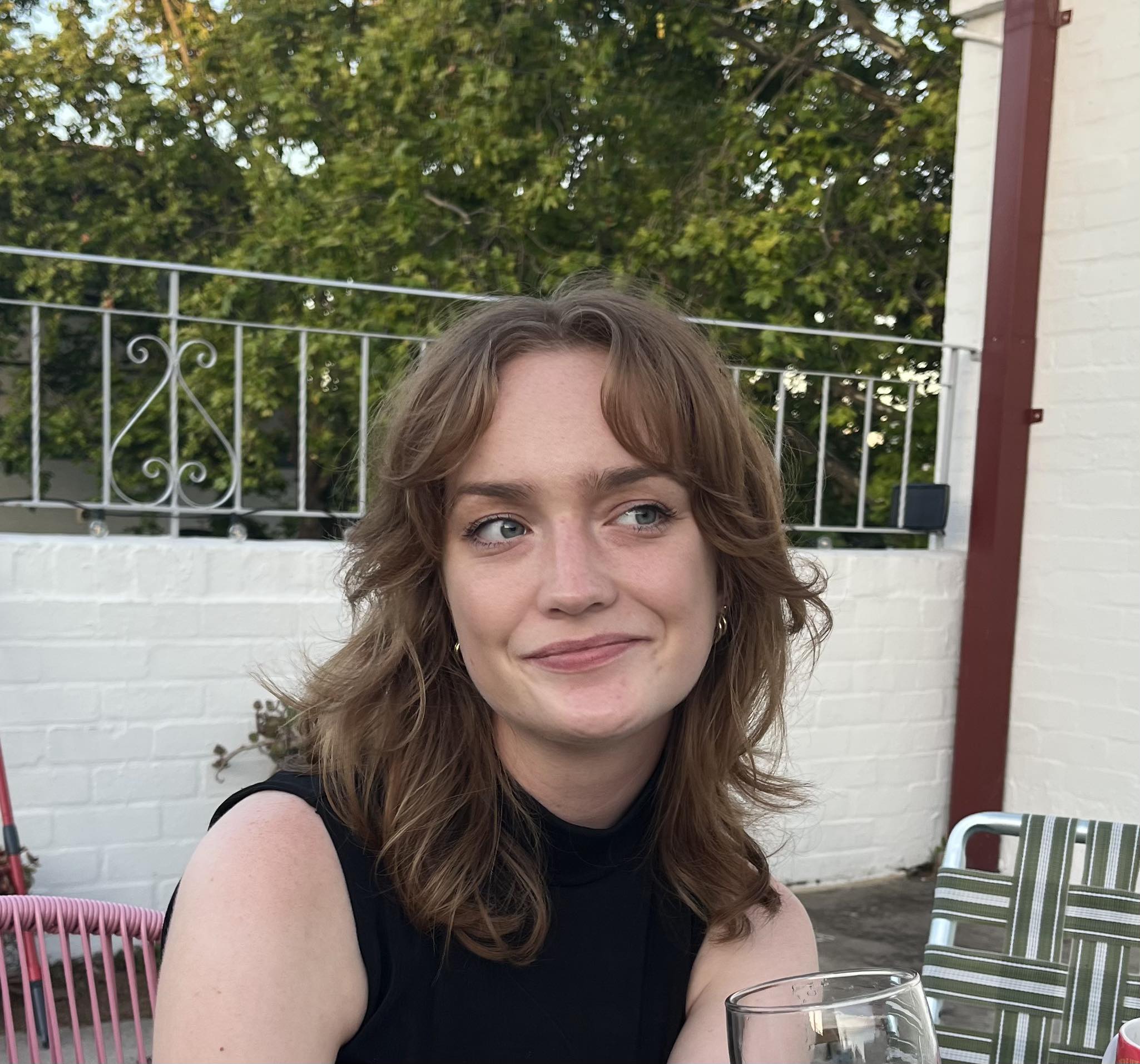 A young woman wearing black singlet top smiles while sitting at an outdoor table