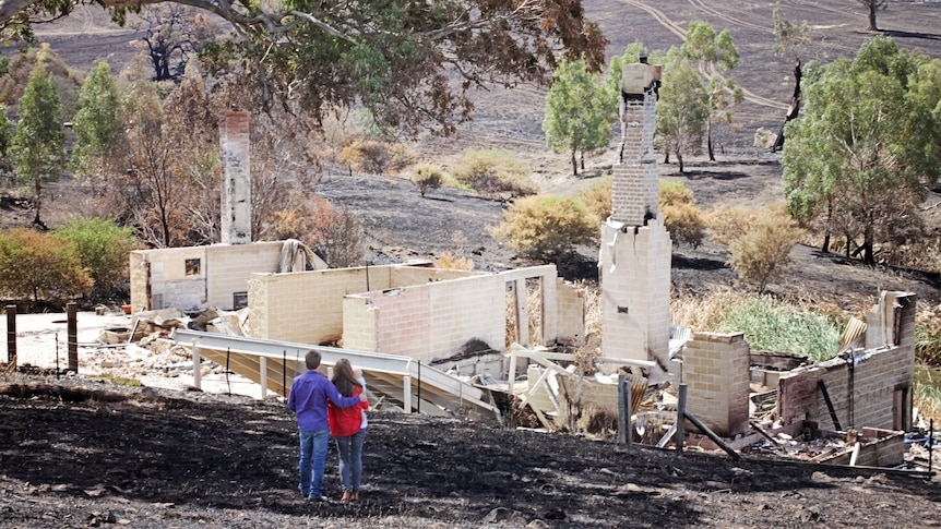 Scott Pape looks at the remains of his bushfire-ravaged home with his family.