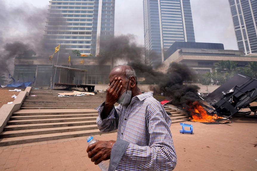 Un hombre de Sri Lanka reacciona a los gases lacrimógenos mientras pasa junto a un incendio