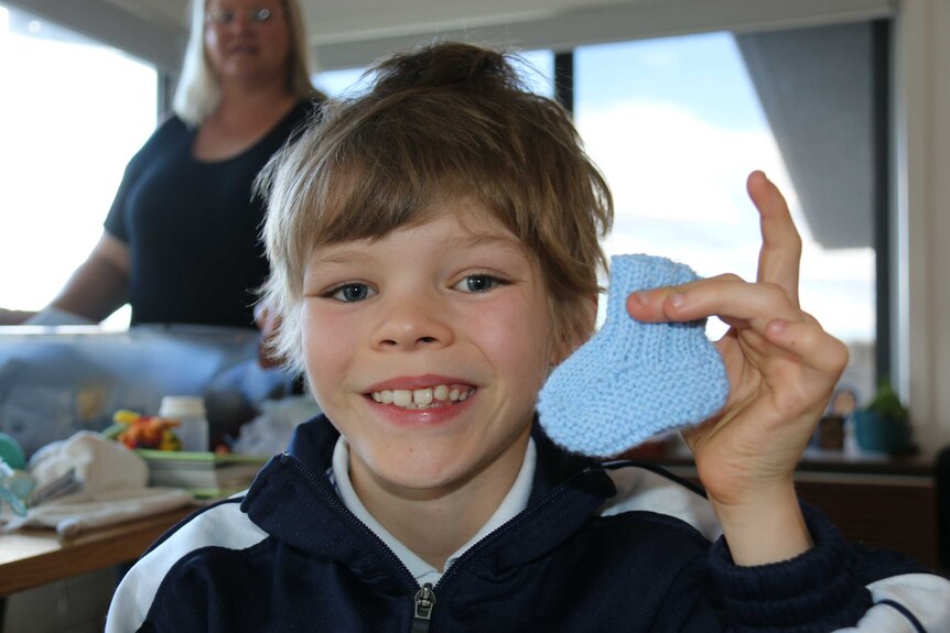 A young boy holds a knitted baby bootie up to the camera.