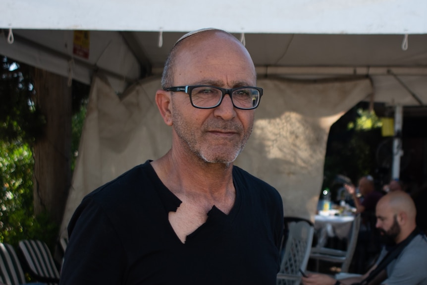 A man in a black t-shirt and glasses stands outside with a tent behind him 