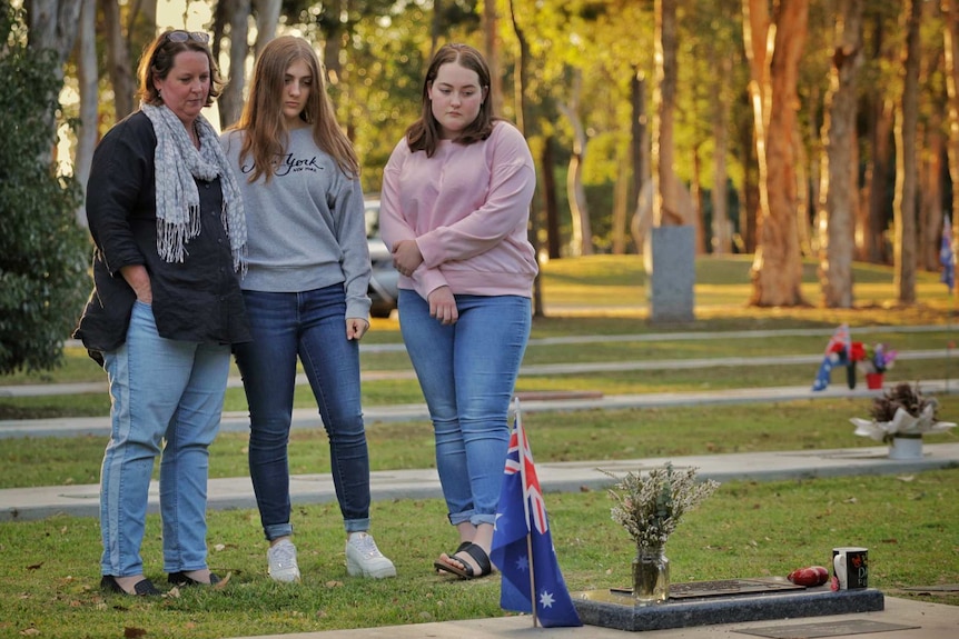 Three women stand beside a grave.