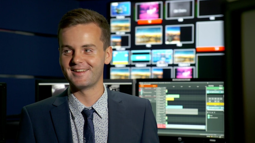 A smiling man in a suit sits in a television control room.