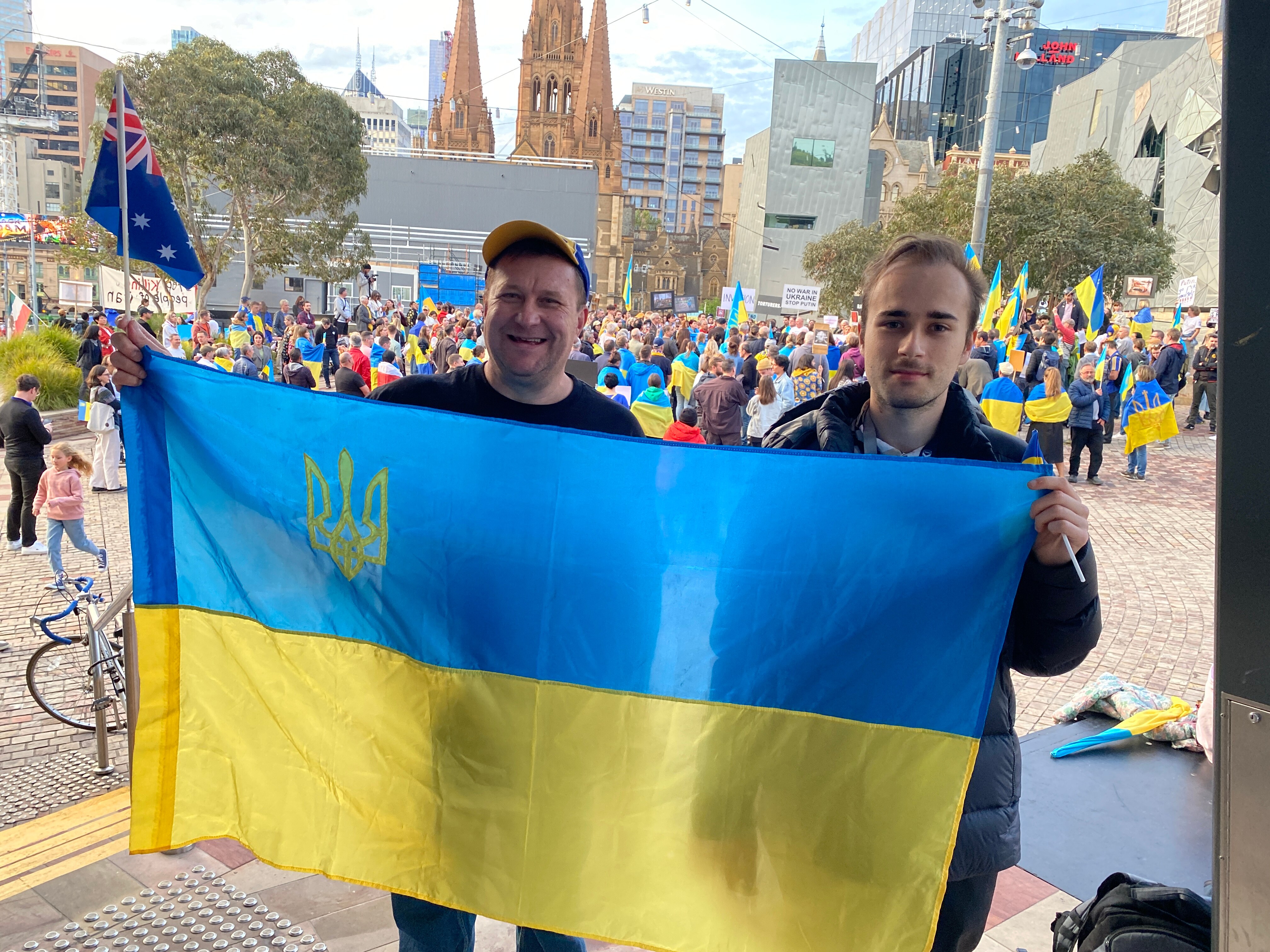 Two men holding a Ukrainian flag. One is wearing a cap and the other has his hair tied back.
