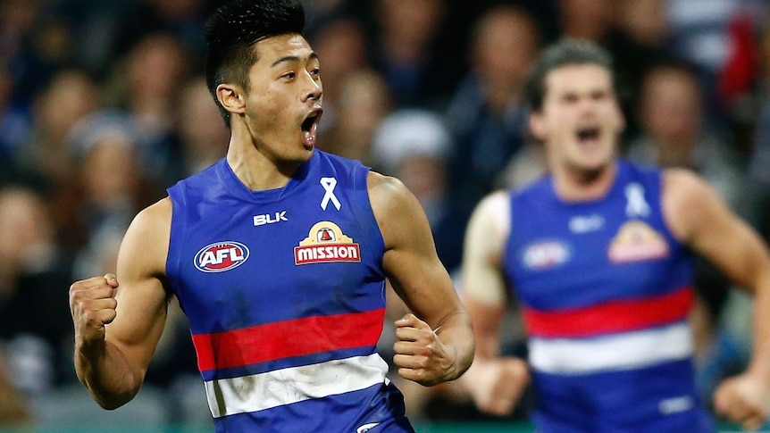 An AFL player in red, white and blue celebrates on the field, with a teammate in the background