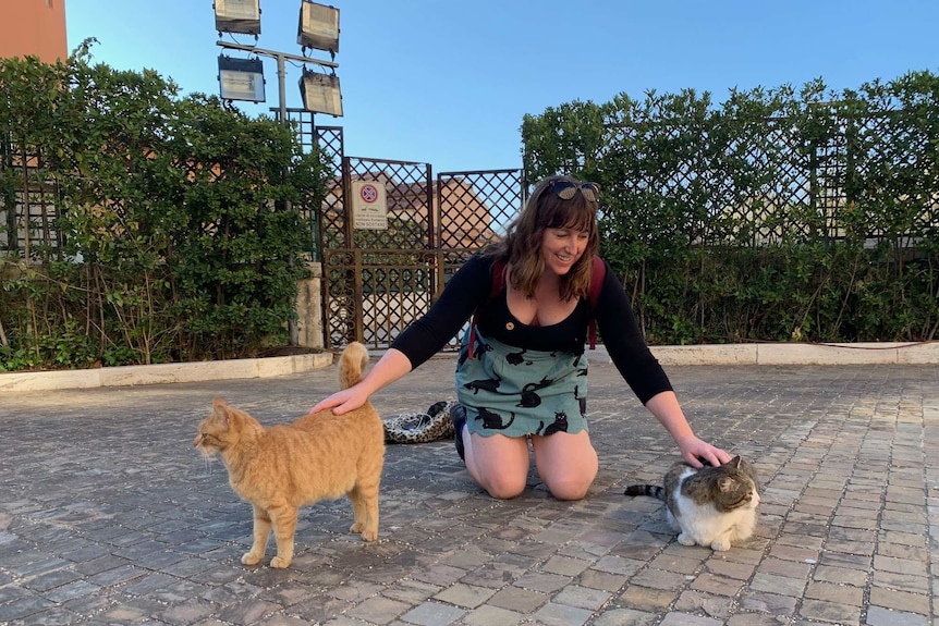 Flip kneeling down patting two cats in Italy