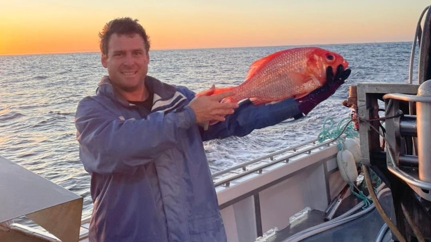 A man holds a fish in two hands on board a vessel at sea