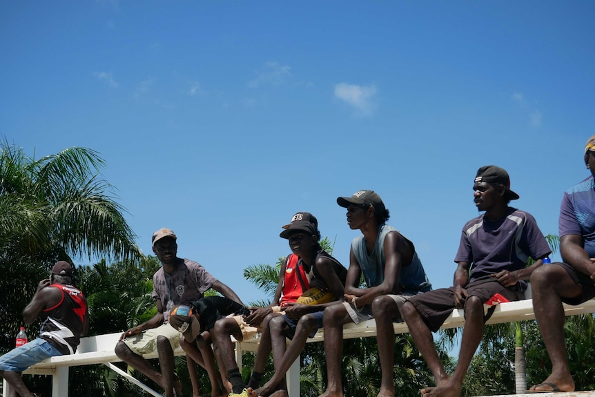 A group of teenagers sit on the bleachers to watch the Tiwi Islands football grand final.