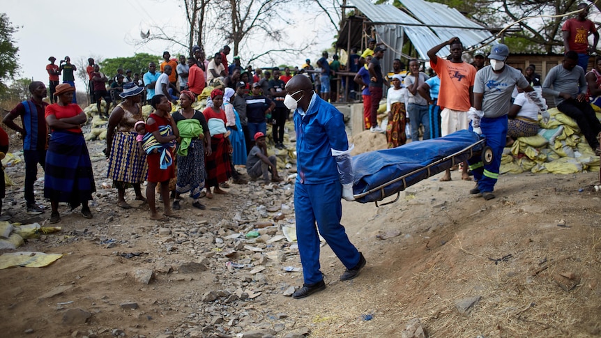 masked and gloved workers take a covered stretcher away