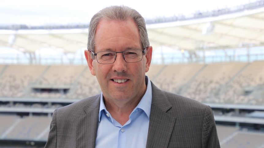 Perth Stadium CEO Mike McKenna stands inside the venue, wearing glasses and a grey jacket.