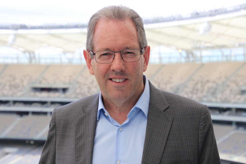 Perth Stadium CEO Mike McKenna stands inside the venue, wearing glasses and a grey jacket.