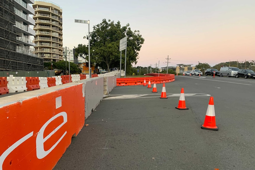 A street lined with cars with orange and white road barricades.