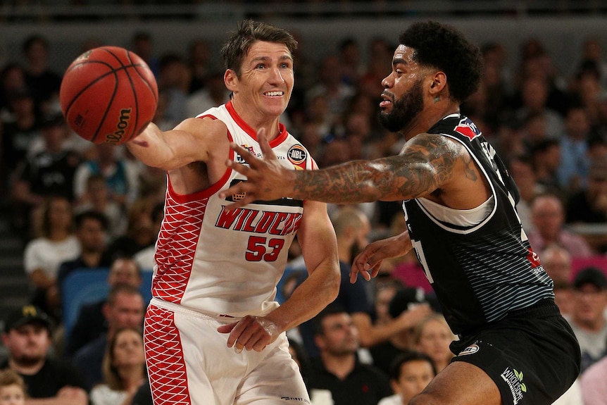 Damian Martin passes a basketball with his right hand while DJ Kennedy tries to stop the pass with his left hand.