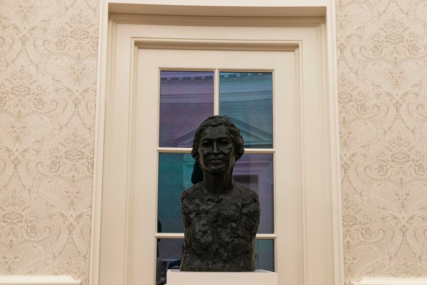 A metal bust of Rosa Parks sits in the Oval Office in front of a white window.