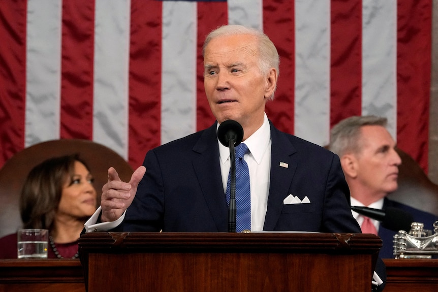 Joe Biden points into the crowd as he delivers his 2023 State of the Union address in front of the American flag