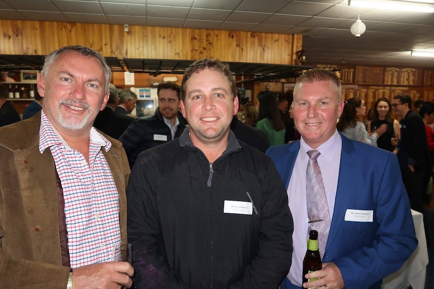 Three men pictured smiling at the camera, with crowds behind them.