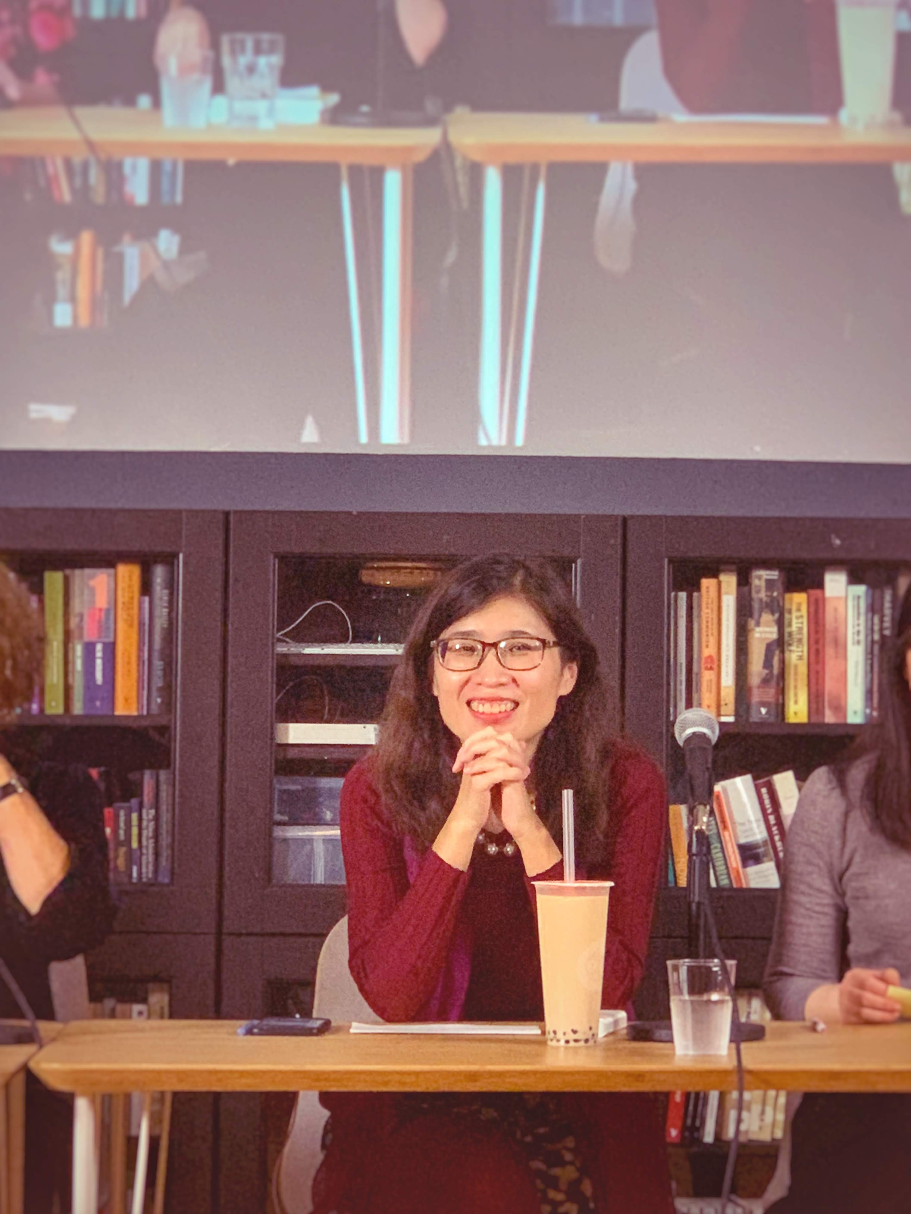 一位女性做在一张桌子前讲话。