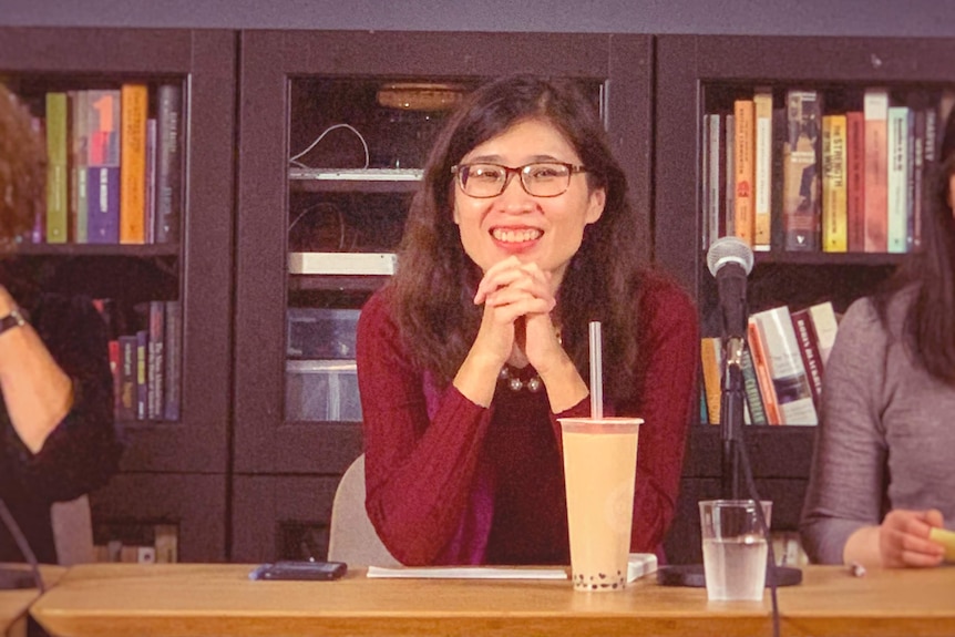 A woman sits in front of a desk smiling.