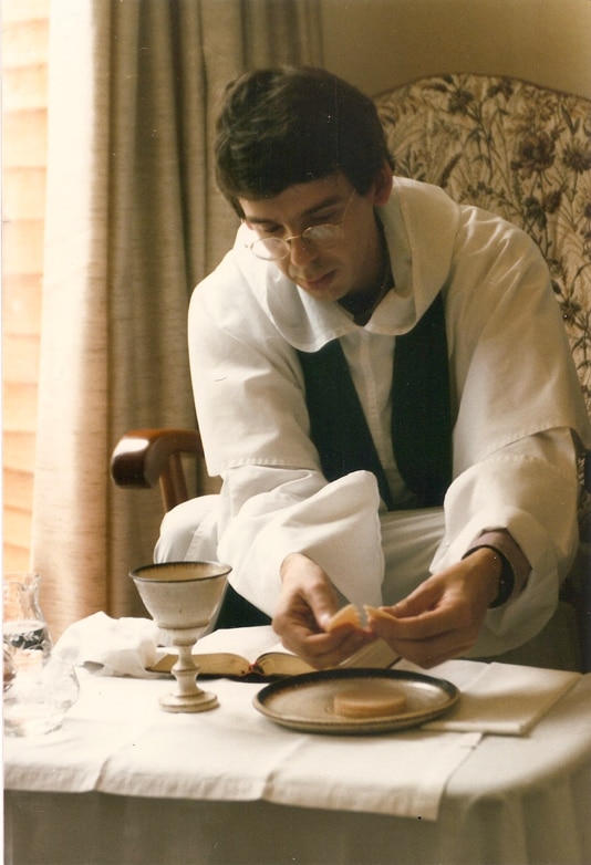 A young man wearing religious robes breaks the sacrament in a Catholic ceremony.