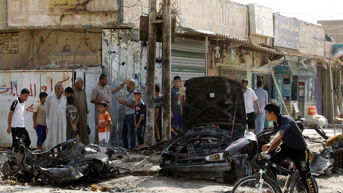 A boy cycles past the burnt-out wreck of a car after a bombing in Baghdad.