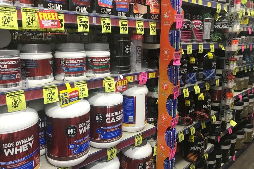 Tubs of supplements line shelves. They have bright price tags hanging below them.