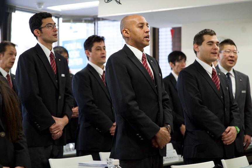 Men in suits stand up in a classroom