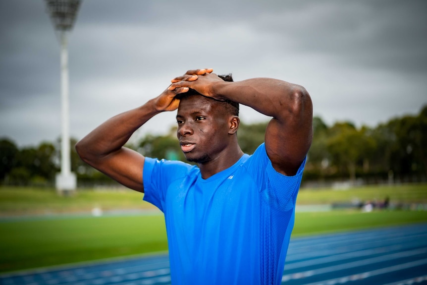 Ismail Dudu Kamara, wearing a blue shirt, puts his hands on his head at an athletics track.