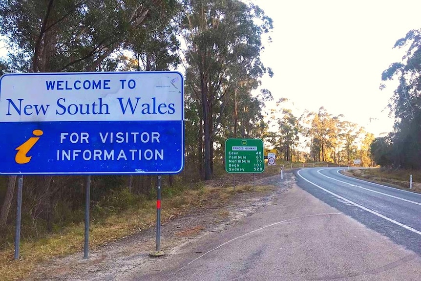 A blue Welcome to New South Wales sign erected next to a highway.