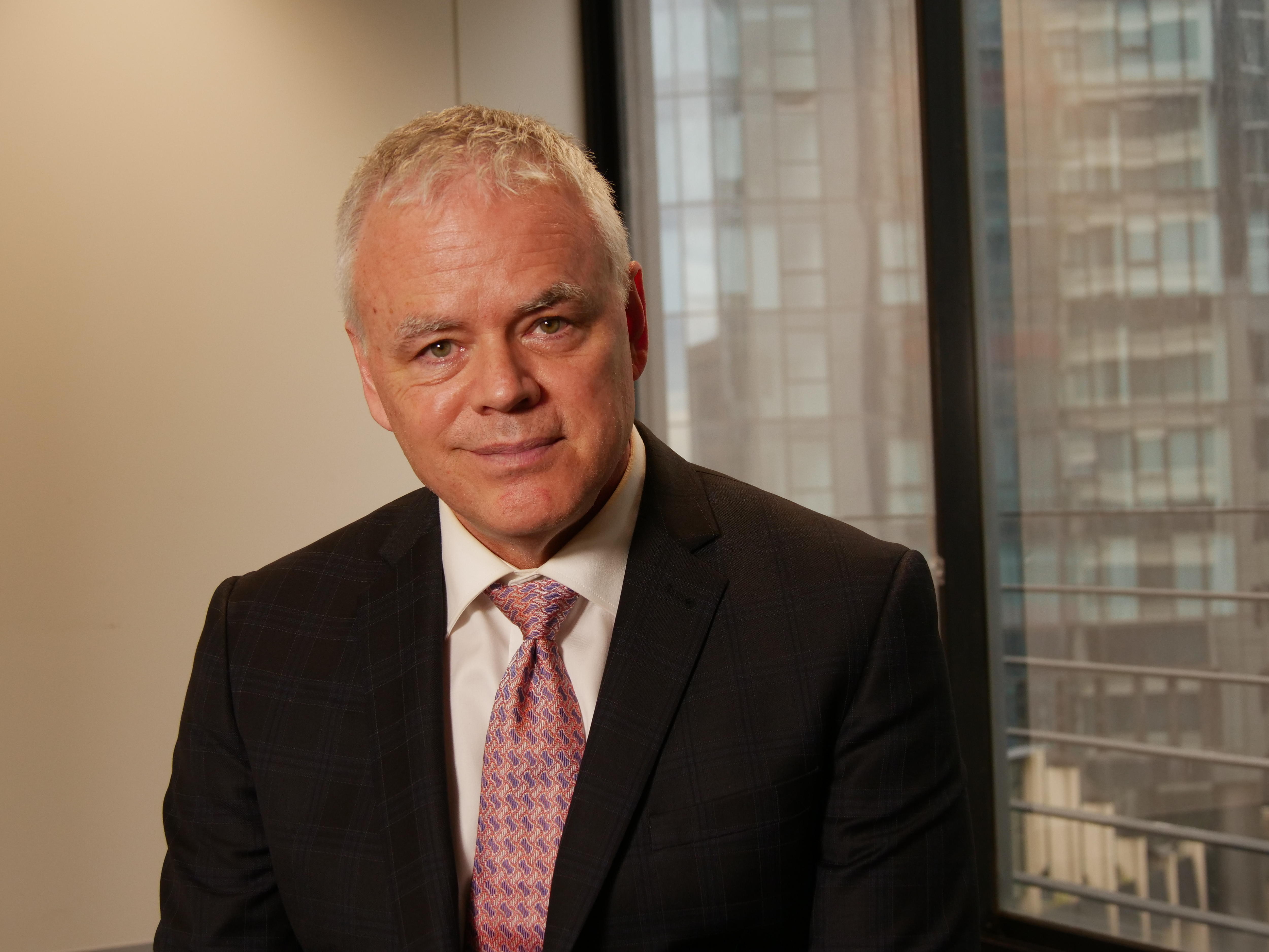 Jim Stanford, dressed in a suit in an office, smiles at the camera