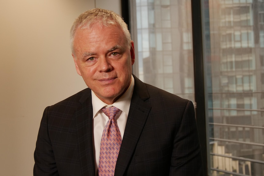 Jim Stanford, dressed in a suit in an office, smiles at the camera