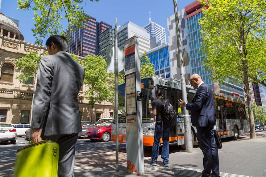 Three men standing at a Melbourne bus stop.