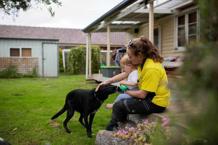 Nikki Fischer and her son, Malakai sitting in backyard patting pet dog