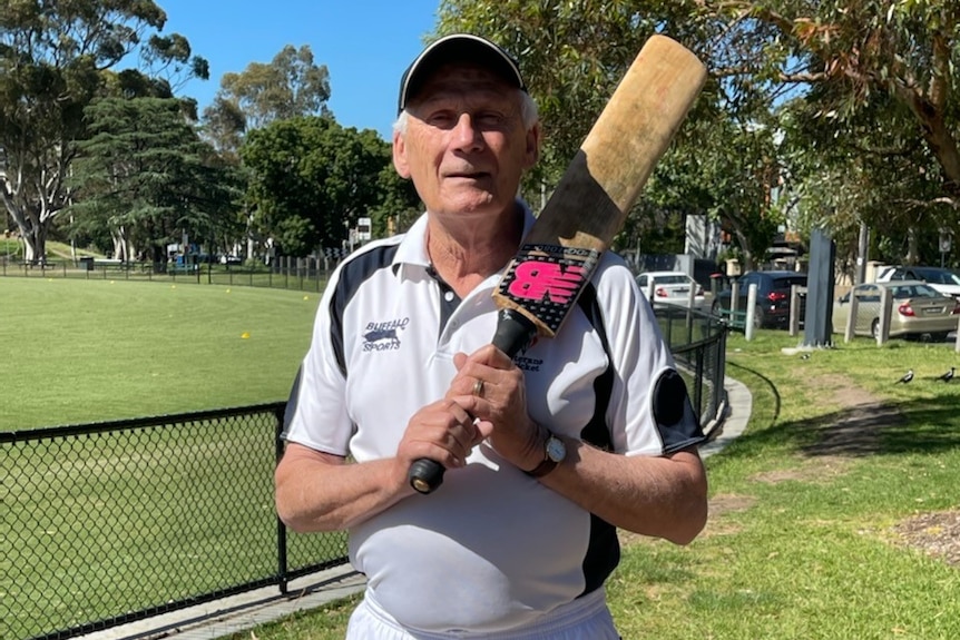 A man in cricket whites holding a cricket bat on his shoulder