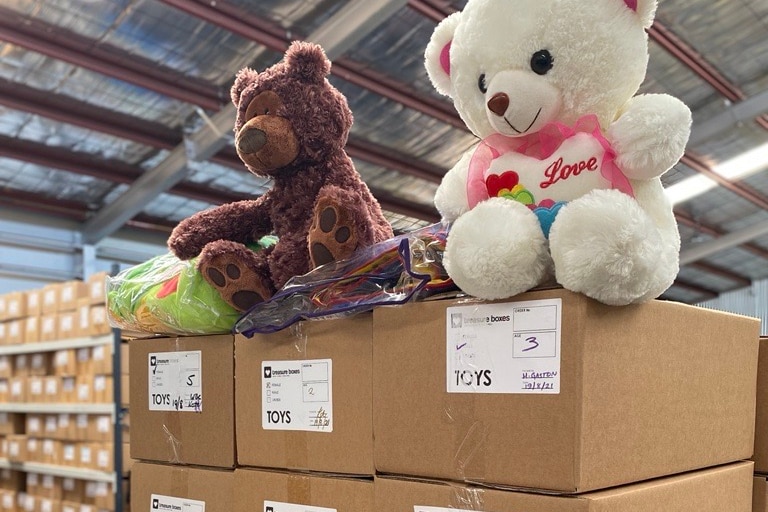 Two teddy bears perched on top of a wall of beige boxes