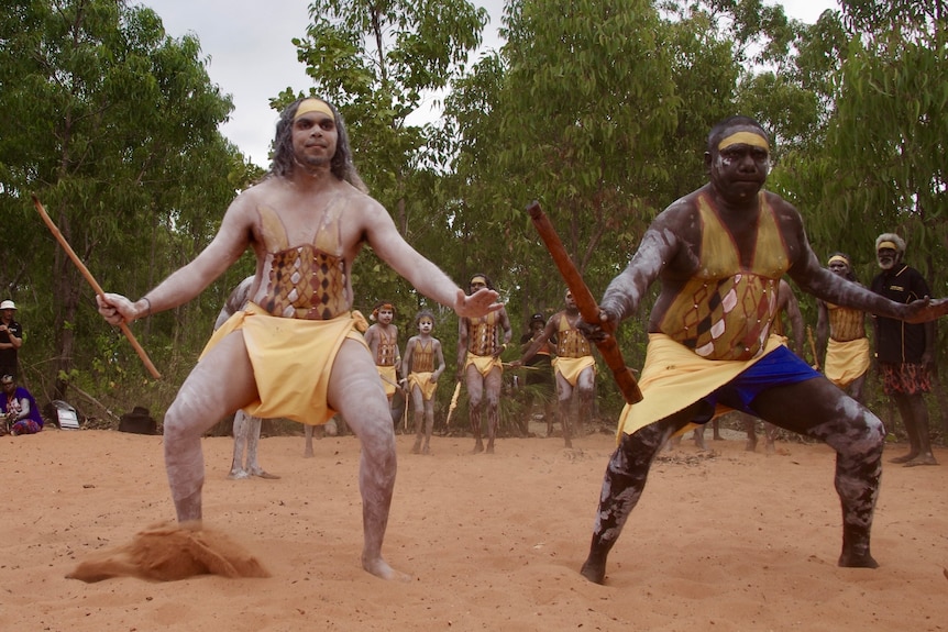 Two indigenous people performing a dance with more dancers in the background. 