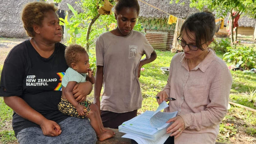 Dr Andrea Burgess sits with two women and a baby in Tanna, Vanuatu explaining the cerebral register. 