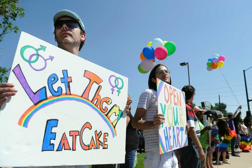 Protesters hold colourful "Let them eat cake" and "open your heart" signs.