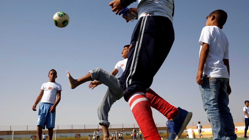 A Syrian child attempts to kick a football in the air while other children look on.