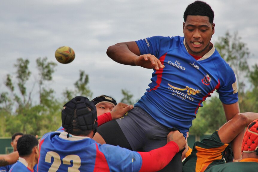 A man in a blue rugby jersey sees the ball fly past him during a lineout jump.