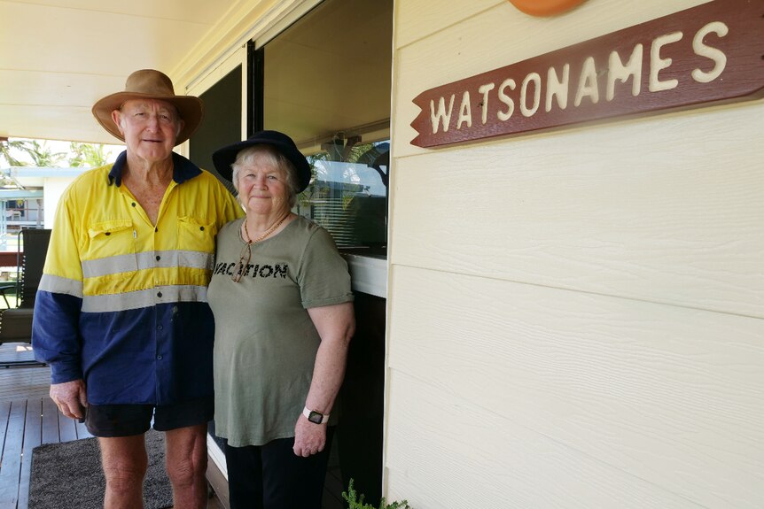 Trevor and Cheryl smiling, standing side by side in front of a glass door, sign that says 'Watsonames' on the right.