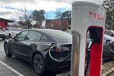 A black electric vehicle hooked up to a Tesla charging station 