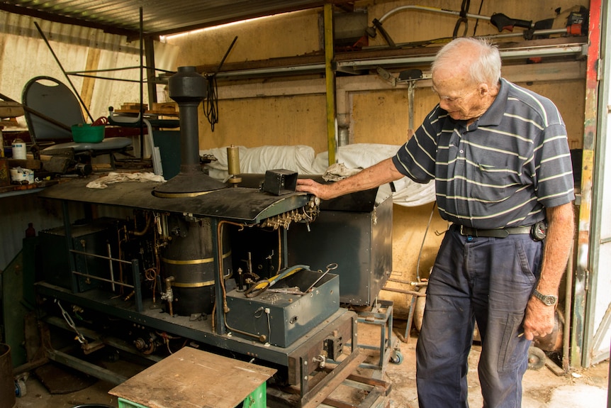 Korean War Veteran stands to the right of a steam engine he is working on.