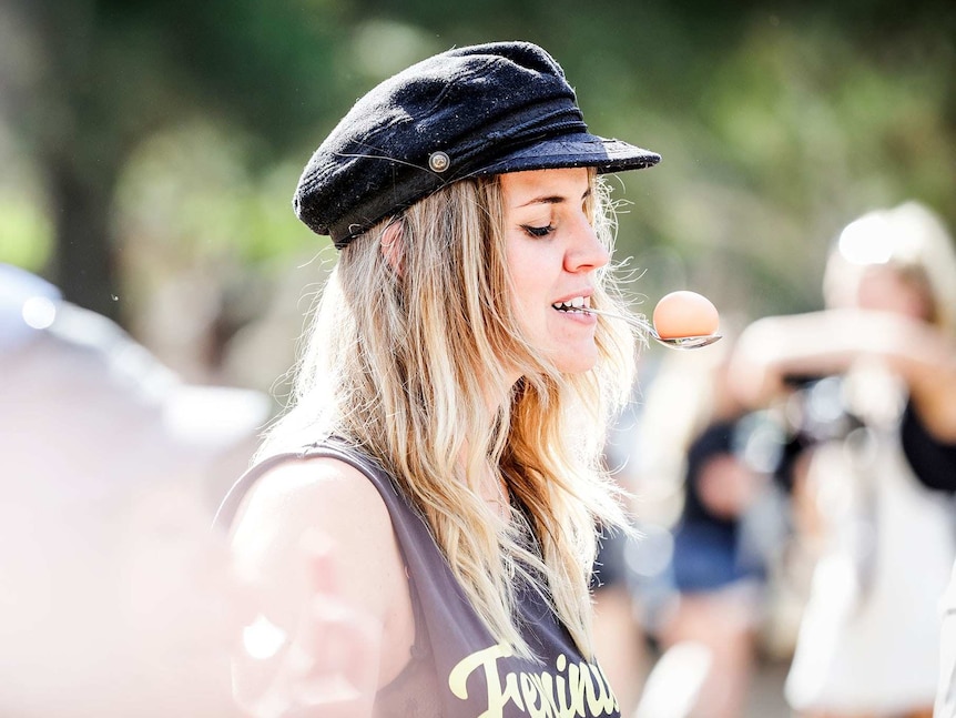 A woman holds an egg on a spoon in her mouth