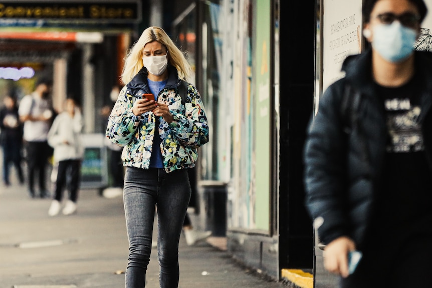 A young woman with a face mask on checks her phone