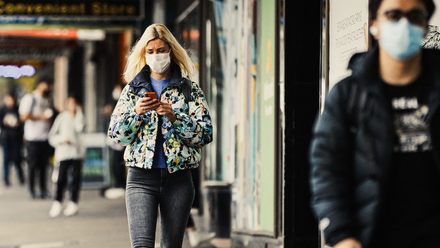 A young woman with a face mask on checks her phone
