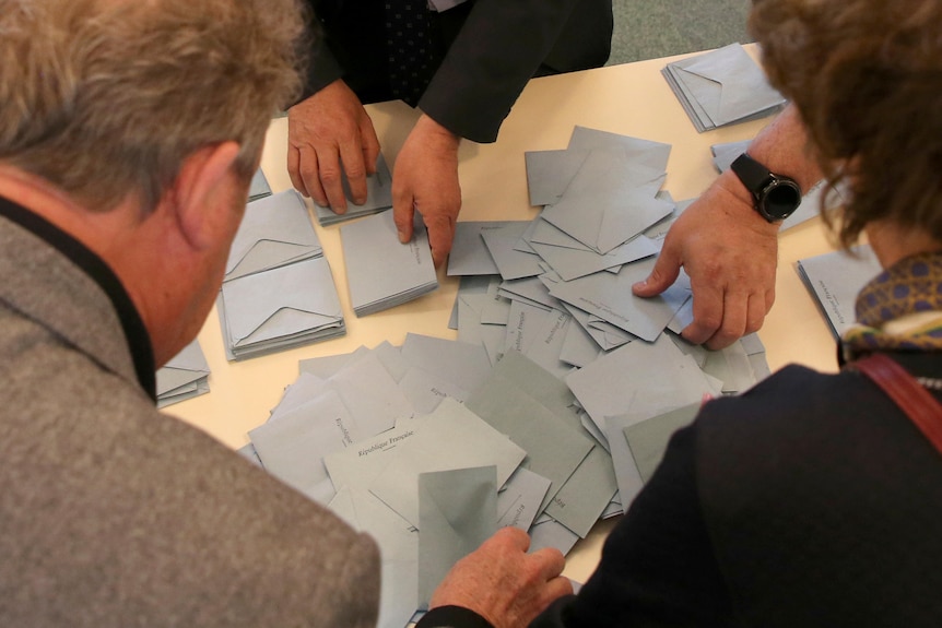 Polling station officials count ballots on a table.