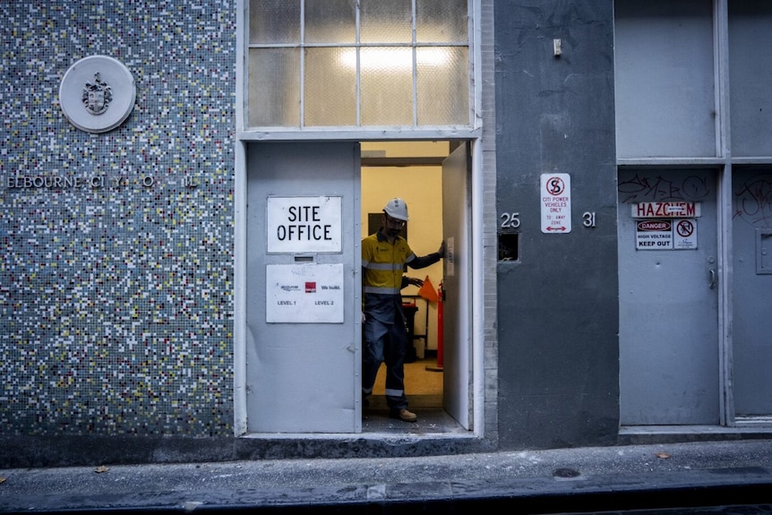 A man wearing a bright CitiPower uniform exits a site office door.